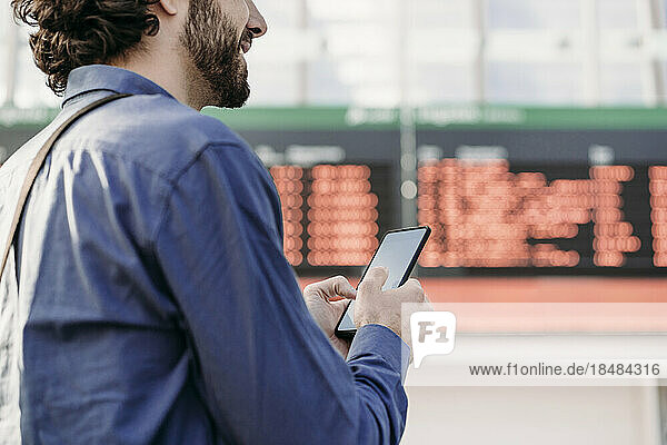 Businessman with mobile phone standing in front of arrival departure board