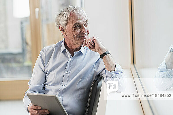 Thoughtful businessman with hand on chin looking out of window at workplace