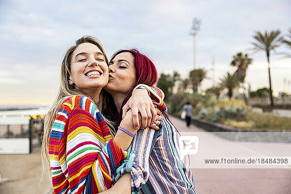 Happy woman kissing friend on cheek at promenade