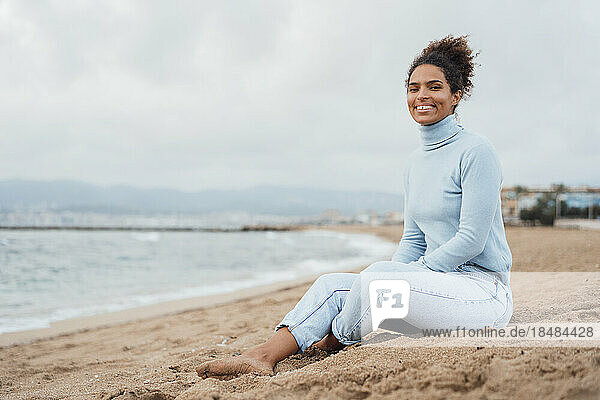 Smiling young woman sitting on sand at beach