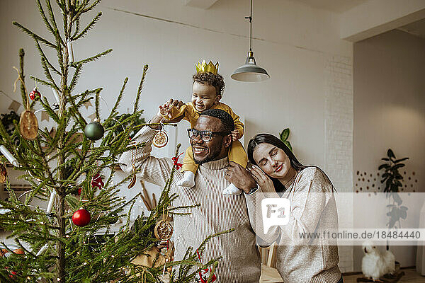 Happy father and mother with daughter touching Christmas ornament at home