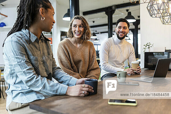 Smiling business people sitting with cup in office cafeteria