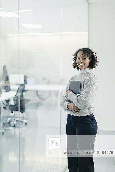 Selbstbewusste Geschäftsfrau mit Laptop an der Glaswand im Büro