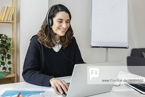 Happy businesswoman wearing headset using laptop at office