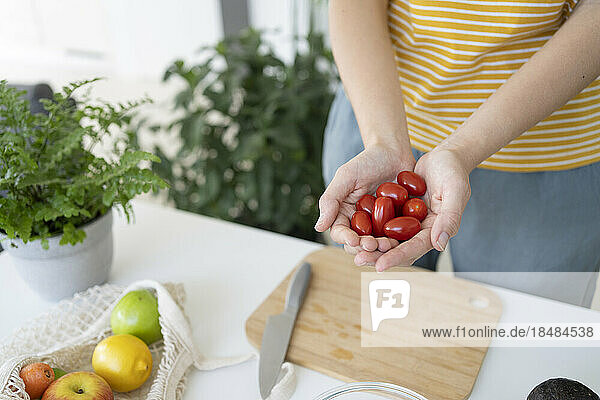 Woman holding cherry tomatoes in cupped hands at home