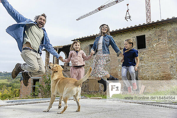 Carefree family jumping by dog outside house