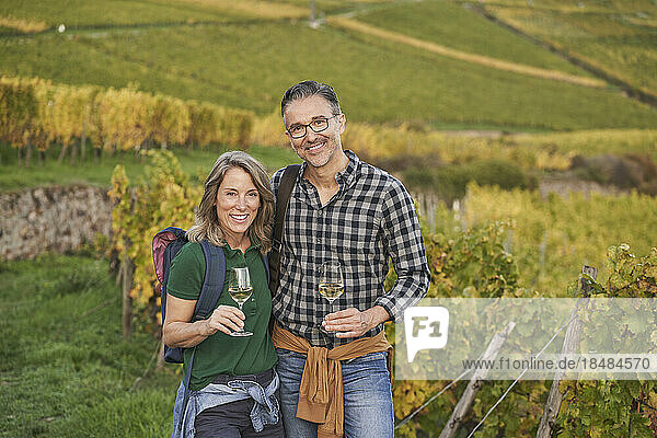 Happy tourists with wineglasses standing in vineyard