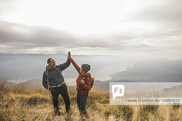 Cheerful man and woman giving high-five to each other standing on mountain