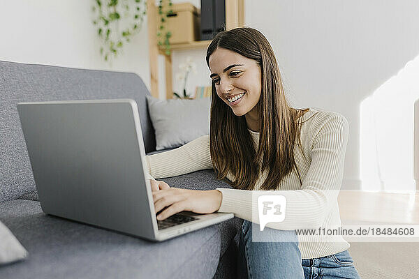 Happy young woman using laptop on sofa at home