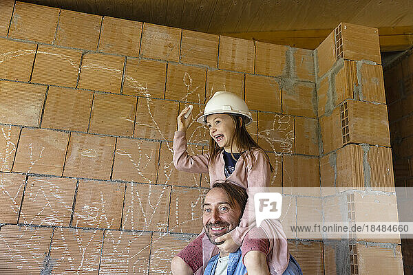 Happy father carrying daughter on shoulders in front of brick wall