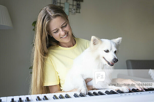 Smiling woman with dog playing piano at home