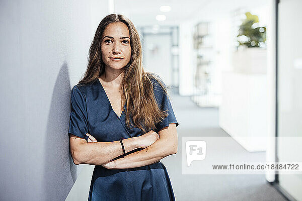 Smiling young businesswoman with arms crossed standing by wall