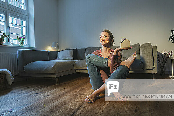 Happy woman with house model doing yoga in living room