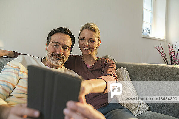 Lächelnde Frau zeigt auf den Tablet-PC  den ein Mann zu Hause hält