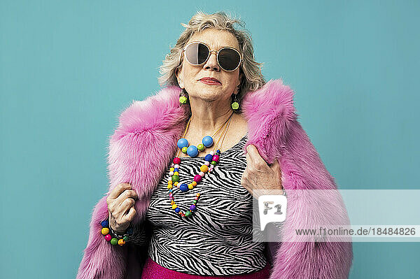 Lächelnde ältere Frau im Pelzmantel vor türkisfarbenem Hintergrund