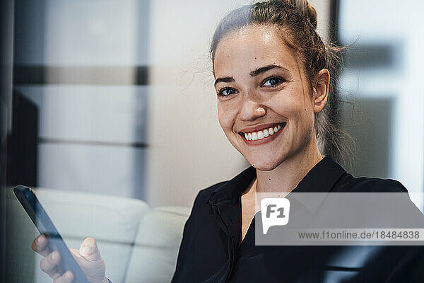 Happy young businesswoman with smart phone seen through glass
