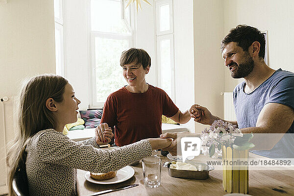 Happy family holding hands sitting at dining table in home