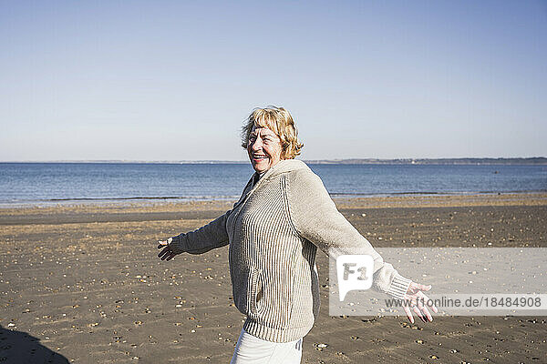 Glückliche ältere Frau mit ausgestreckten Armen  die am Strand spaziert