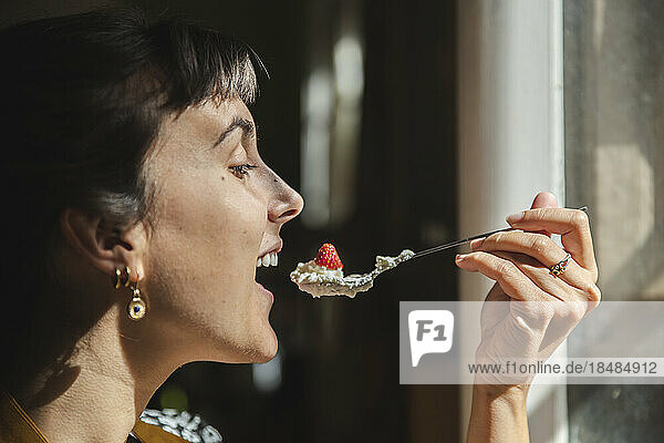 Young woman eating spoon of strawberries and cream