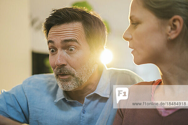 Mature man with raised eyebrows by wife at home