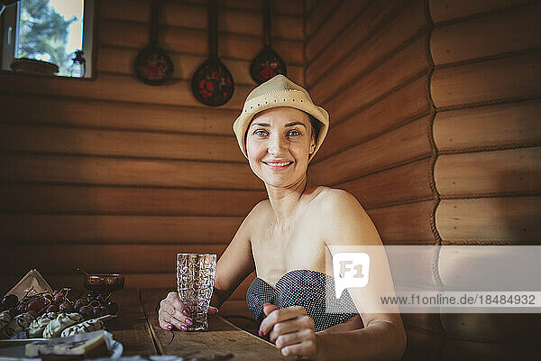 Lächelnde Frau mit Trinkglas sitzt am Tisch in der Sauna
