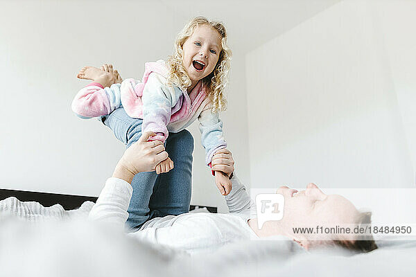 Happy daughter having fun and playing with father on bed at home