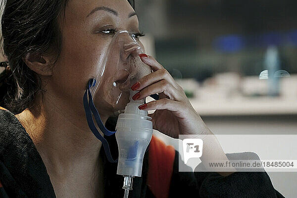 Woman inhaling through inhaler mask at home