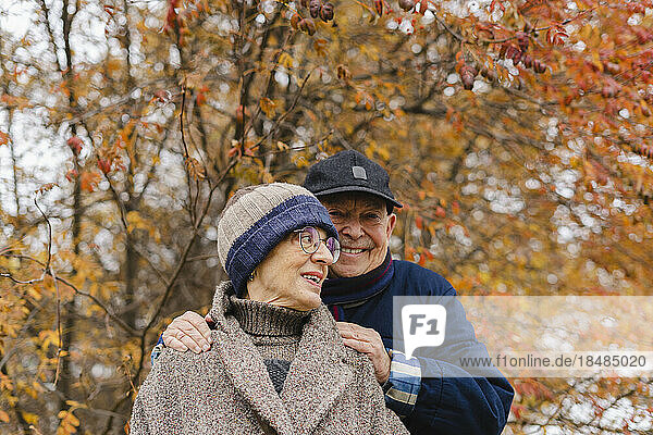 Glücklicher älterer Mann mit den Händen auf den Schultern einer Frau unter einem Baum