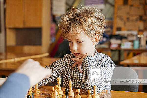 Boy with hand on chin playing chess at sports club