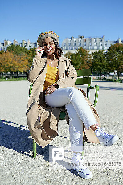 Happy young woman with beret sitting on chair in park