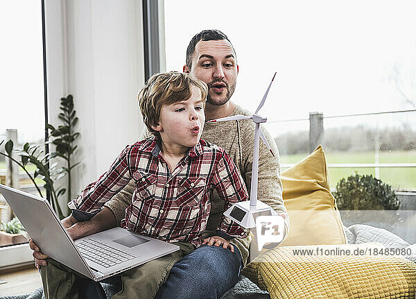 Father and son blowing wind turbine at home