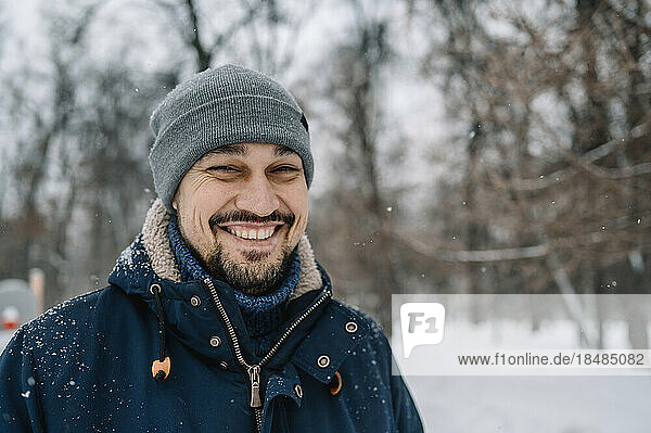 Happy man wearing knit hat enjoying snowfall