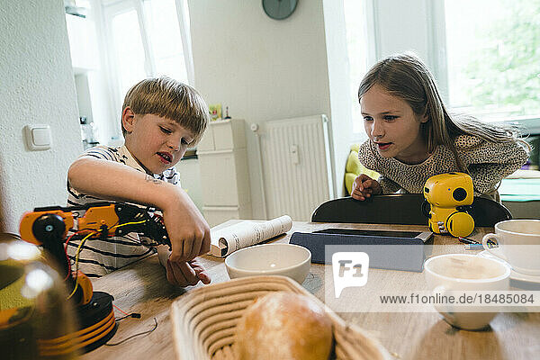Girl looking at brother playing with robotic model at home