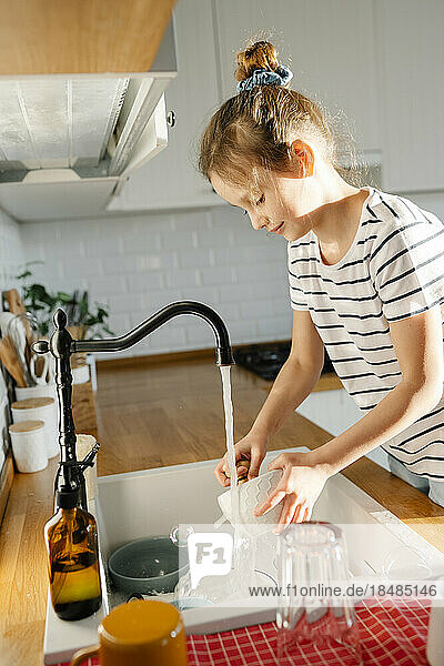 Girl washing dishes in sink at home