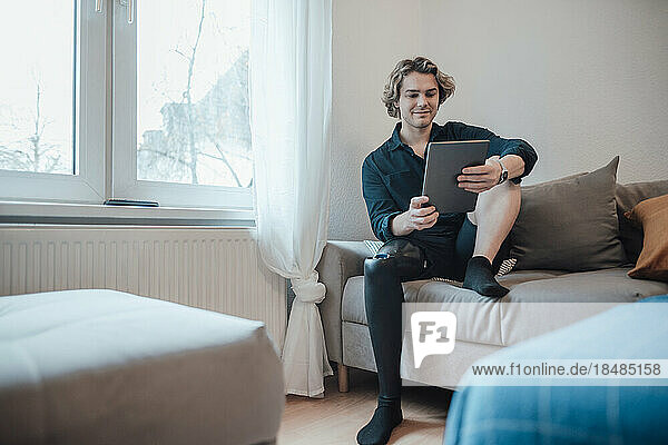 Junger Mann sitzt zu Hause auf dem Sofa und benutzt einen Tablet-PC