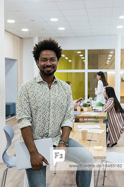 Porträt eines lächelnden Geschäftsmannes im Büro mit Kollegen im Hintergrund