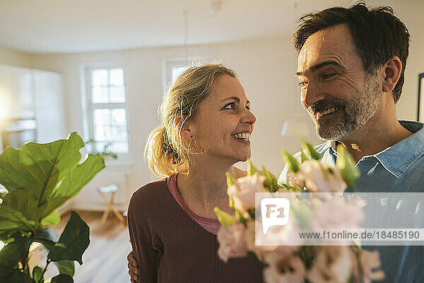 Happy husband surprising wife with flowers at home