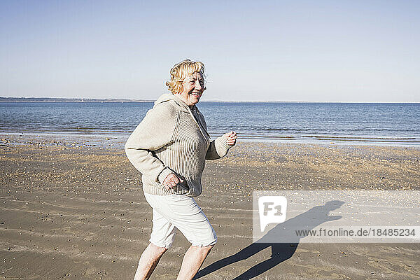 Smiling elderly woman running by sea at beach on vacation