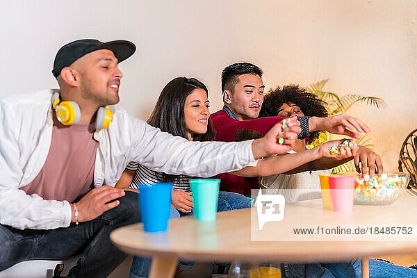 Gruppenbild von multiethnischen Freunden  die auf dem Sofa Popcorn essen und Limonade trinken. alle Popcorn essen