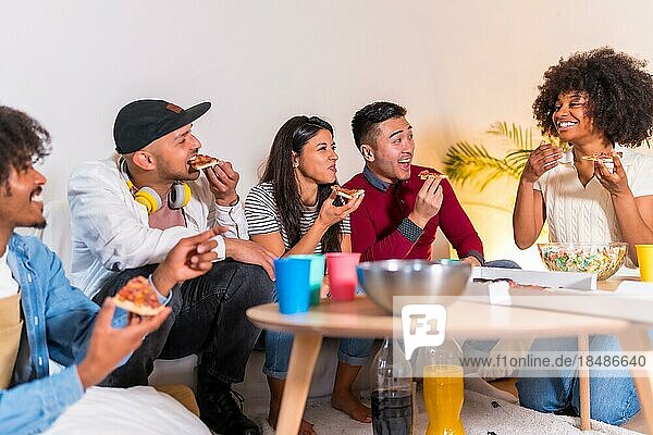 Gruppe multiethnischer Freunde auf einem Sofa  die bei einer Party zu Hause Pizza essen und Limonade trinken  Pizza essen und Witze erzählen