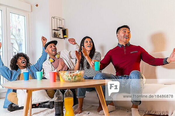 Gruppe multiethnischer Freunde auf einem Sofa  die auf einer Hausparty Pizza essen und alkoholfreie Getränke trinken und das Mädchen mit der Pizza willkommen heißen