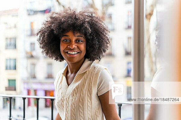 Portrait of a young black ethnic woman with afro hair on a balcony at home smiling  everyday situation  at sunset looking at camera
