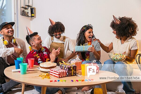 Gruppe von Freunden bei einer Geburtstagsfeier auf dem Sofa zu Hause  die lächelnd die Geschenke überreichen und das Geburtstagskind überraschen
