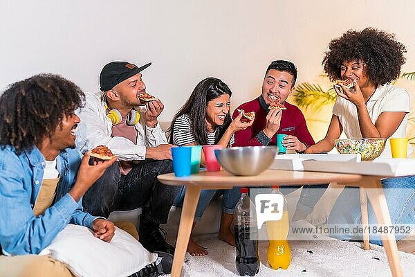 Eine Gruppe multiethnischer Freunde sitzt auf einem Sofa  isst Pizza und trinkt Limonade bei einer Hausparty  isst Pizza und erzählt lustige Geschichten