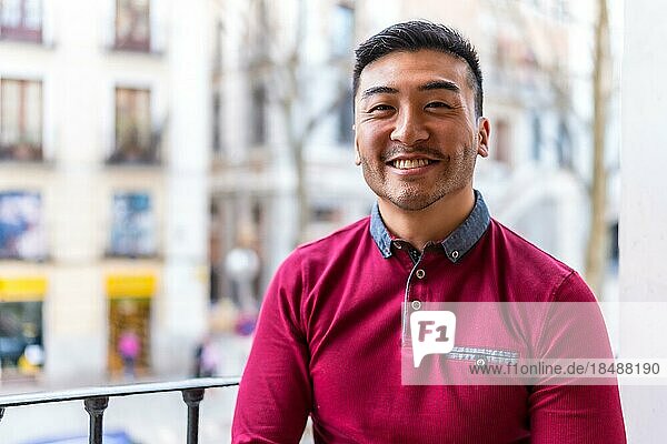 Porträt eines jungen chinesischen Mannes auf einem Balkon zu Hause  lächelnd  Alltagssituation  Wohnung