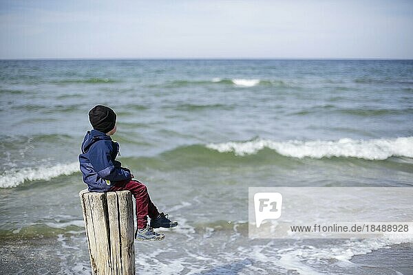 Symbolfoto zum Thema Einsamkeit in der Kindheit. Ein Kind sitzt allein auf einem Holzpfosten am Meer. Arenshoop  20.04.2022  Arenshoop  Deutschland  Europa