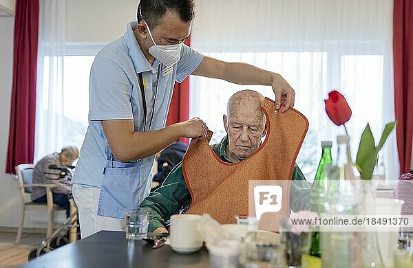 Carer puts a bib on a man in a nursing home  Heidelberg  Germany  Europe