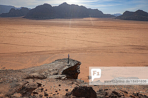 Eine Person steht auf einem Felsen über der weiten Ebene der Wüste Wadi Rum  UNESCO-Weltkulturerbe  Jordanien  Naher Osten