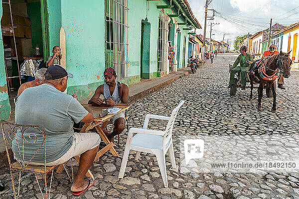 Domino-Spiel am Tante-Emma-Laden  während ein Pferdewagen auf Kopfsteinpflaster vorbeifährt  Trinidad  Kuba  Westindien  Karibik  Mittelamerika