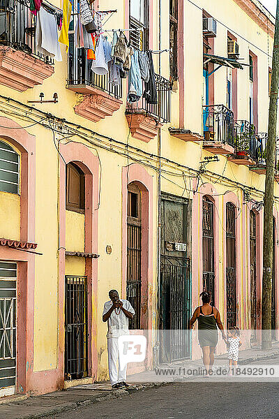 Man lights cigar in typical backstreet  colourful washing draped on balconies  Old Havana  Cuba  West Indies  Caribbean  Central America